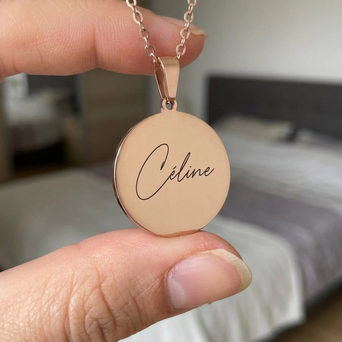 Collier gravé prénom Céline, pendentif rond or rose tenu entre deux doigts